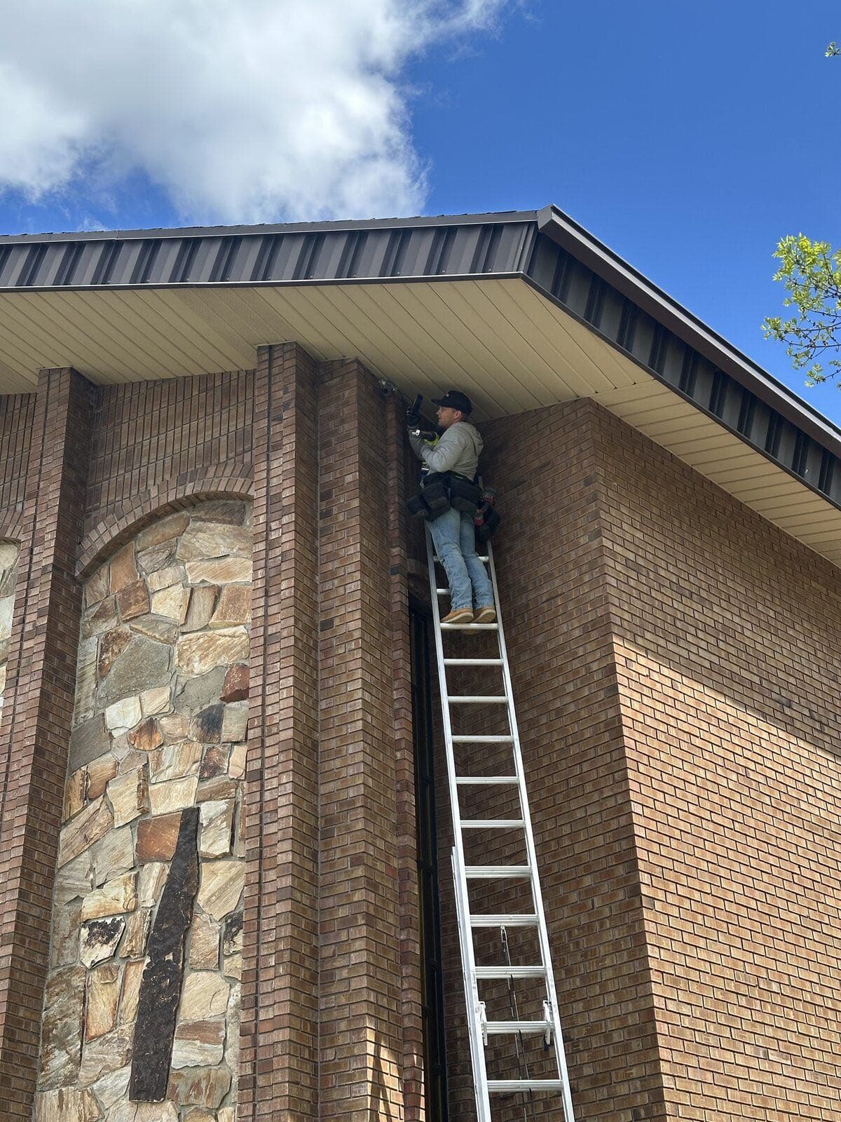 Technician on a ladder sealing an entry point where the soffit meets the brick