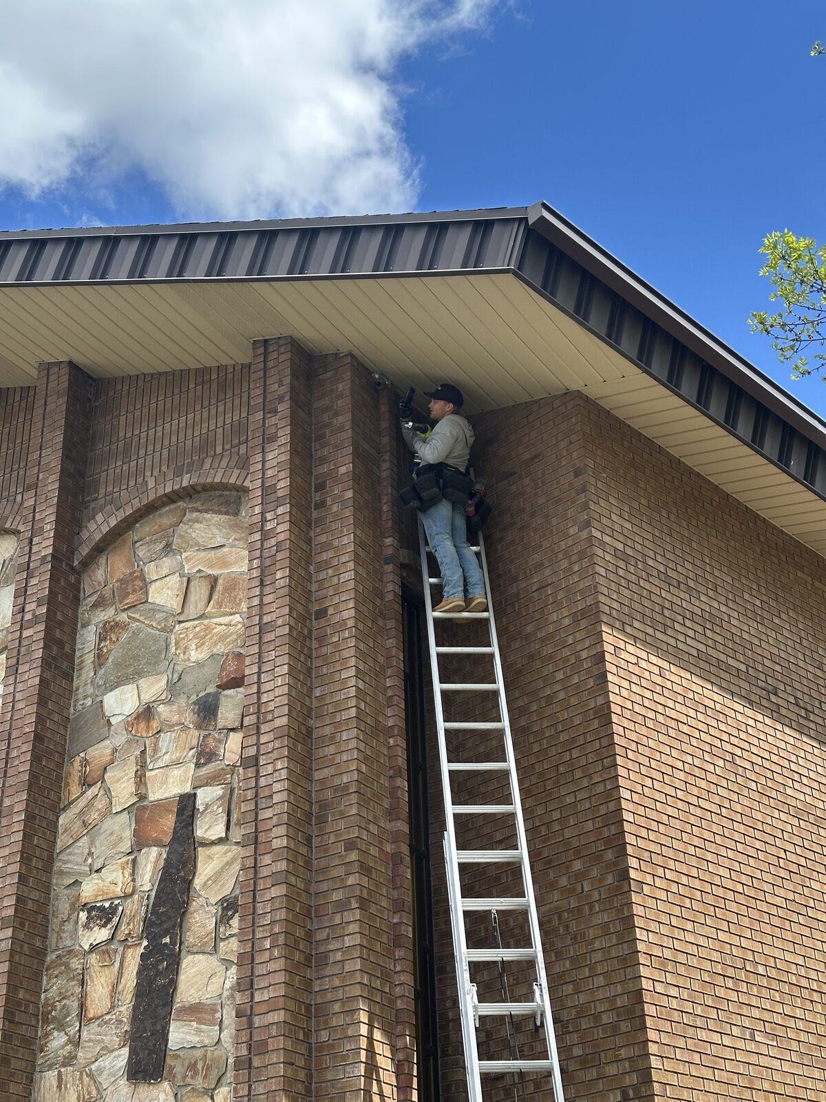 Technician on a ladder sealing a gap where the soffit meets the exterior brick